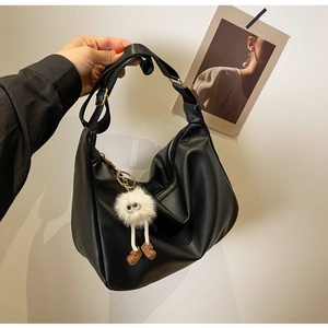 Détail du sac hobo en cuir grainé noir avec un porte-clé monstre en peluche blanc