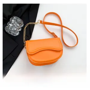 Detail of bright orange saddle bag with metal chain strap beside a phone for scale