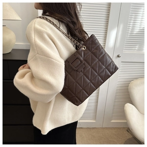 Detail of coffee brown quilted tote bag with chain strap worn by a model in a cozy setting