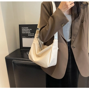 Sac hobo minimaliste en similicuir crème avec large bandoulière porté par un mannequin