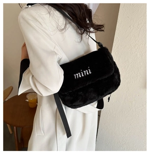 Détail du sac bandoulière en peluche noire avec broderie mini blanche porté par un mannequin