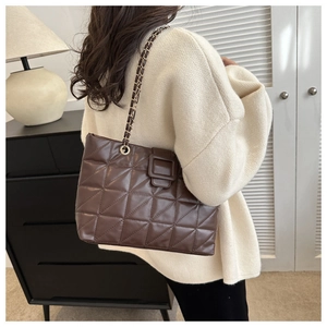 Detail of a brown quilted tote bag showing a side view on a model with chain straps