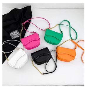 Flat lay of multiple minimalist saddle bags in vibrant colors with gold chain straps