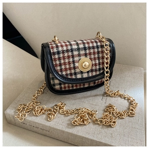 Detail of tweed crossbody bag featuring a golden relief buckle and metal chain strap