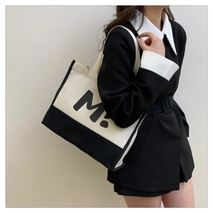 Détail du sac cabas en toile montrant la texture, l'imprimé lettre M et la bandoulière