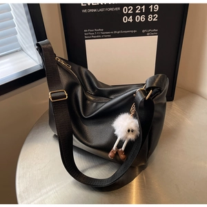 Détail d'un sac bandoulière en cuir grainé noir avec sangle large et breloque peluche