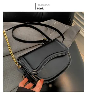 Detail of a black saddle bag featuring scalloped edges and a gold chain strap on fabric