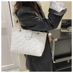 Detailed close-up of white quilted tote bag featuring gold chain strap and square buckle