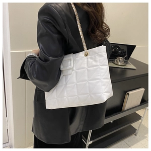 Close-up of a white quilted tote bag with metal chain strap and large buckle detail
