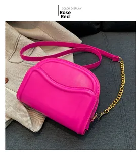Detail view of a rose red saddle bag with gold metal chain on a textured fabric background