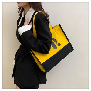 Gros plan du grand sac cabas en toile bicolore avec lettrage logo jaune sur fond noir