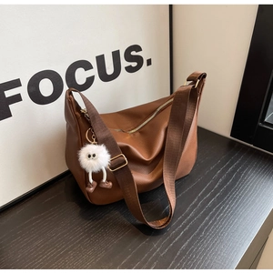 Détail d'un sac demi-lune en cuir marron avec un pompon blanc et des accessoires dorés