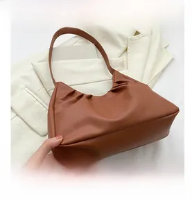 Detail shot of a brown pleated hobo bag with soft leather texture on a cream blazer