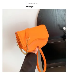 Detail of an orange saddle bag with gold chain strap held by a model in a minimal setting