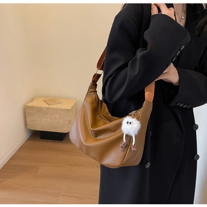 Sac hobo en cuir marron avec large bandoulière orange et breloque en peluche blanche