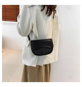 Detail of black matte saddle bag featuring fine stitching and gold chain strap