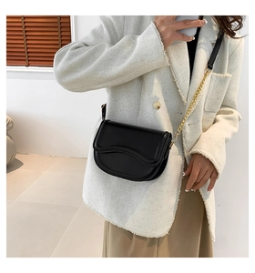 Detail of black saddle bag with wavy embossed flap and gold chain strap on a model