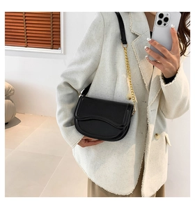 Detail of black saddle bag with wavy flap and gold chain strap shown on model