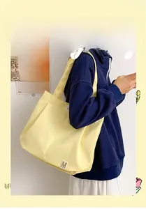 Detail of a bright yellow tote bag with an M logo badge worn by a model in casual style