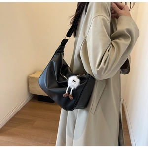 Gros plan sur le sac en croissant noir à texture litchi et petit charme en peluche blanc