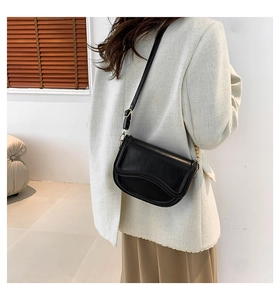 Detail of a black minimalist saddle bag with wave-edge flap worn by a model in a blazer