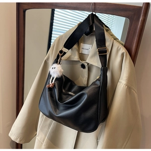 Détail du sac bandoulière en cuir grainé noir avec sangle large et pendentif blanc