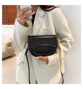 Detail view of black saddle bag with wavy flap and gold chain on a tweed jacket