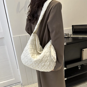 Close-up of beige quilted tote bag with heart stitching and mini pouch on model