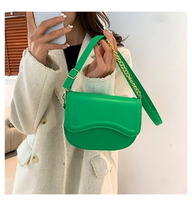Detail of bright green saddle bag with scalloped flap and gold chain strap on a model