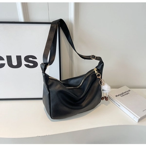 Détail d'un sac demi-lune en cuir noir avec breloque en peluche et bandoulière