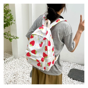 Detail view of a white backpack with red strawberry prints worn by a model in soft lighting