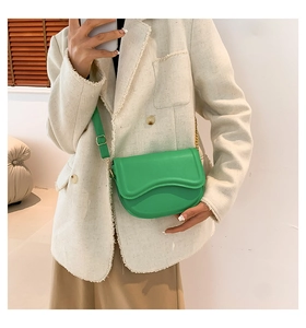 Detail of a bright green faux leather saddle bag with golden hardware and wavy flap design