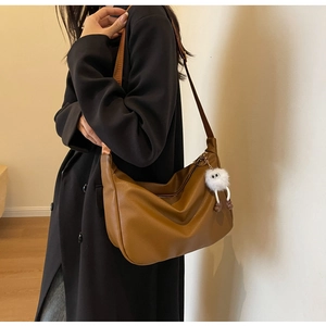 Sac hobo en cuir marron avec breloque peluche portée sur un manteau d'hiver noir