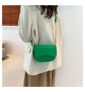 Model wearing a vibrant green saddle bag with gold chain strap on a shoulder