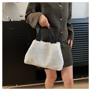 Detail of white faux fur tote bag with black strap held by model in tweed suit