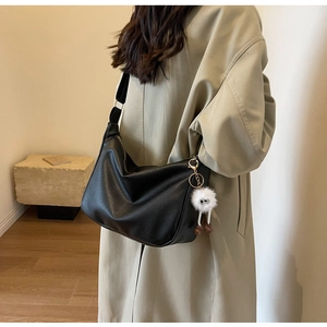 Vue détaillée du sac noir grainé avec bandoulière large et pendentif de poupée en peluche
