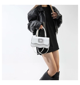 Détail d'un sac à main blanc avec boucle en cristal et bord ondulé sur un mannequin