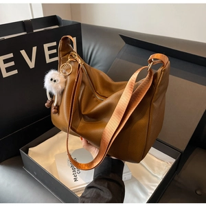 Vue détaillée du sac cabas en cuir marron avec breloque peluche sur une boîte cadeau