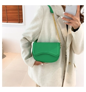 Detail view of a bright green saddle bag with gold chain and wavy flap leather texture