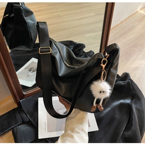 Détail d'un sac hobo en cuir grainé noir avec bandoulière large et breloque peluche