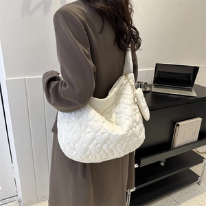 Close-up of white heart quilted tote bag with matching heart charm shown on model