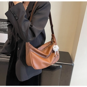 Détail du sac croissant en cuir marron avec breloque peluche sur un mannequin en blazer