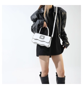 Détail d'un sac blanc à bords ondulés avec boucle en strass porté sur une veste noire