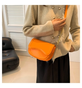 Bright orange crossbody bag with wave flap and gold chain strap on a chic fashion model