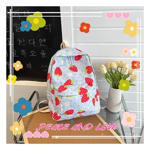 Close-up of light blue canvas backpack featuring red strawberry and daisy patterns