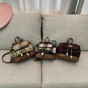 Detail of three vintage tweed mini backpacks in green, black, and red plaid on a soft sofa