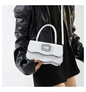 Détail d'un sac à main en cuir blanc avec boucle ornée de cristaux et bordure ondulée