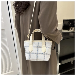 Detail view of plaid tweed tote bag with cream leather straps on a dark coat