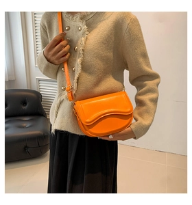Detail of vibrant orange saddle bag with wavy flap design and adjustable shoulder strap