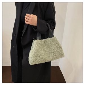 Close-up of a soft light green plush bucket bag with black webbing straps held by a model